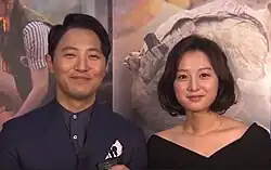 Actors Jin Goo and Kim Ji-won pose side-by-side in front of a promotional backdrop for "Descendants of the Sun"