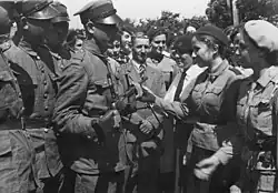 Crowd scene outdoors showing Polish soldiers at a 1938 ceremony, where a late-series Browning wz. 1928 with anti-aircraft spiderweb sight and an ergonomic buttstock is presented.