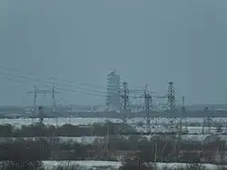 Power lines on snowy flat terrain. In the distance is a large pagoda under construction