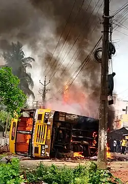 Photograph of a burning yellow school bus, lying on in its side