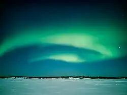 Curtains of greenish light in the night sky over a flat, snowy landscape