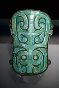 A photo of a bronze plaque in a museum inlaid with an animistic turquoise design