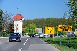Yellow road sign in Brežice, Slovenia pointing to Spodnja. There are also cars on the road and a two story building with a red roof.