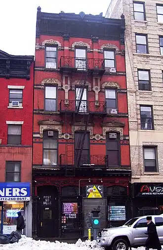 Exterior of four-story red brick building houses the Pyramid Club at street level, its entrance marked by a yellow triangular sign, flanked by neighboring shops and snowy sidewalks