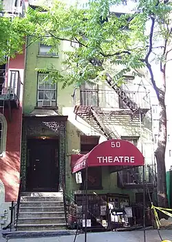 Red awning covering the sidewalk and stairs down to the basement entrance of the theater; immediately to the left, stairs leading up to the first-floor entrance to the rest of the 3-story tenement building that houses the theatre.