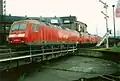 Three locomotives in a line. All are red with grey roofs an a grey stripe around the base of the body. The first has a DB Cargo logo on the side, the second only DB