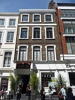 The façade of a narrow brick building with white trim with a modernised ground floor; the entrance has a sign above in big Chinese characters; the building is flanked tightly by two other buildings