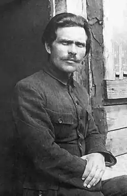 Portrait photograph of Nestor Makhno, wearing a moustache and a black suit, resting in a doorway