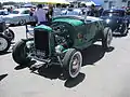 Hi-boy Deuce roadster with a flathead V8 (with factory head and exhaust but aftermarket alternator ignition and dual-carb intake), dropped tube axle, and drum brakes.