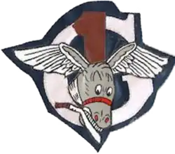 upper case letter gee, white on a blue background, imposed on it is a red number one, imposed on both is the grey head of a smiling mule, with eagle wings spread from each ear and holding a machete in its teeth
