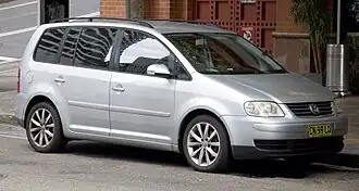 Front-three-quarter view of a five-door car with a raised roofline, flush headlights, front foglamps, door mirrors with integrated turning indicator lights, alloy wheels, and bars for attaching a roof rack