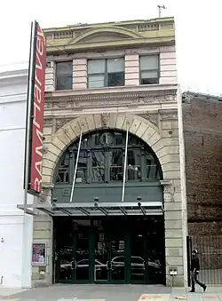 The entrance to a building in an urban environment. Above the eave of the entrance hangs a sign that reads "RAM Harvey".
