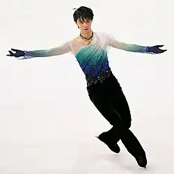 Hanyu skates in a costume where the top goes through a gradation from white to blue to black. The front has many draped folds that are accentuated with rhinestones