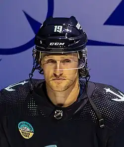 Ice hockey player in a Seattle Kraken jersey and helmet in front of a blue background