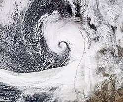 Satellite image of the Western United States and Pacific Ocean, with the states of the US shown in thin black lines. The November 2024 bomb cyclone is visible as a comma-shaped formation of clouds off the west coast of North America.