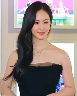 Yuri wearing a strapless black dress. Her hair is on the side. She's wearing a necklace.