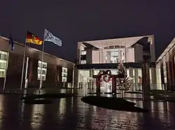 The Federal Chancellery in Berlin during the presidency, with a flag featuring the logo of the council presidency flying in front of the building, next to a flag of Germany and one of Europe