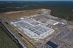 Gigafactory Berlin-Brandenburg in Grünheide, on the edge of a highway with an industrial park in the distance