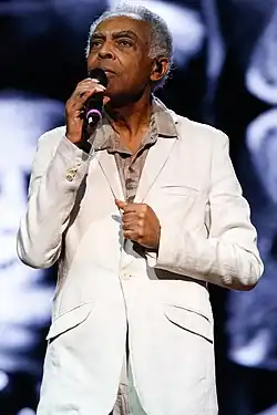 A man with dreadlocks holding a guitar and standing behind a microphone stand.