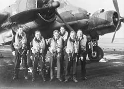 Six young men wearing flying suits standing in front of a World War II-era twin engined monoplane