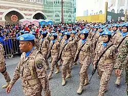 Joint Malaysian Armed Forces personnel attached to United Nations peacekeeping duties marching during Merdeka Day. They are seen wearing UN blue berets with the desert digital camouflage combat uniform, which has been in use since 2013 and remains the current pattern.