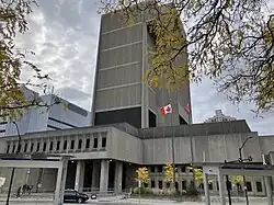 This is a photo of the Ontario Court of Justice regional building in London, Ontario. It is a large imposing concrete structure done in a brutalist style. It is grey and clouding in the background.