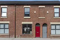A colour photo of a red-bricked house with boarded up windows and doors