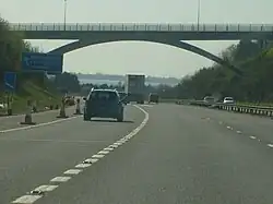 multi-carriageway road with vehicles passing under an elevated roadway and distant view of sea beyond