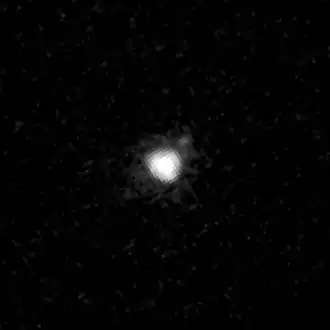 A black-and-white photograph of Achlys and its moon taken by the Hubble Space Telescope on 2 December 2005. In the black backdrop of space, Achlys appears a large white dot at the center while its moon appears as a small gray dot to the upper right of Achlys.