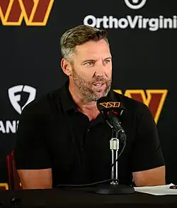 Photo of a man speaking to a microphone at a press conference.