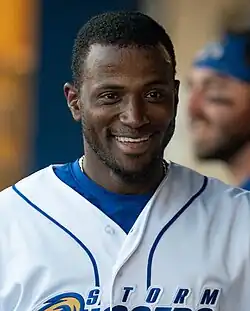 Adeiny Hechavarría smiling in a white Omaha Storm Chasers uniform in the dugout in 2023