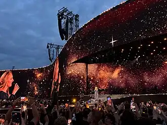 Adele sings into her microphone, dressed in a navy Dior gown