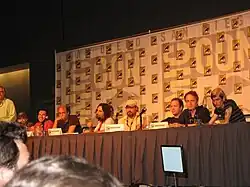A long table with a group of white men sitting behind it, each with a microphone in front of them