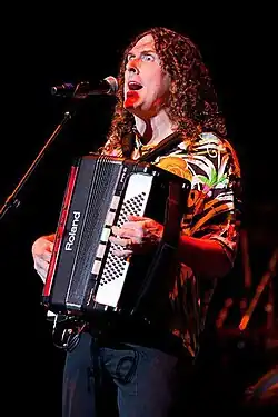 "Weird Al" Yankovic in front of the microphone while performing on his accordion at a 2010 concert tour.