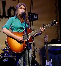 Young woman playing an acoustic guitar on stage, singing into a microphone