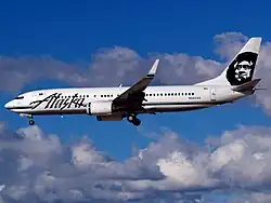 Left side view of an aircraft on final approach, with partly cloudy skies in the background.