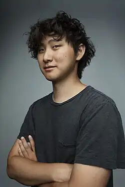 Studio portrait of Wang wearing a dark gray T-shirt, with a gray background