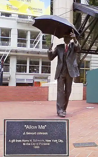 A bronze statue of a man in a business suit; in one hand he is holding an umbrella, while his other arm is extended.