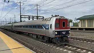 A silver railroad car with a blue stripe over the windows. At one end, an angular green shape covers the stripe.