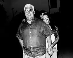Black-and-white image of Mitch in the foreground, smiling and looking at the camera; behind him is Winehouse, leaning on his shoulder