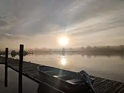 Foggy day on the Anacostia River. View from a dock with the sun in the sky, a duck on the water, and a motorboat on the dock.