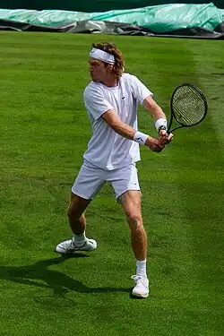 Andrey Rublev wearing white hitting a tennis ball on a grass court at the 2023 Wimbledon Championships