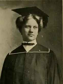 A young woman facing the camera dressed in traditional college graduation cap and gown
