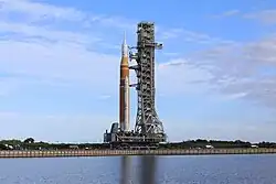 The Space Launch System, a 322-foot-tall rocket with orange insulation and white paint, being transported on Crawler-Transporter 2 to its launch pad, January 17, 2026