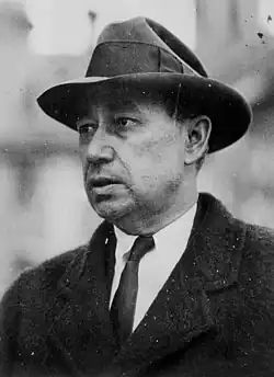Photo of Austin dressed in outdoor business attire: a Homberg-style hat, white business shirt and tie, and a winter coat.