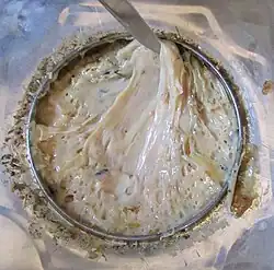 Close-up of a metal container filled with a thick beige substance stirred with a metal blade.