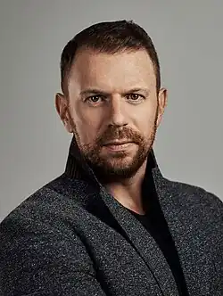 Portrait photo of a white man with brown hair; he is wearing dark clothing and looking into the camera