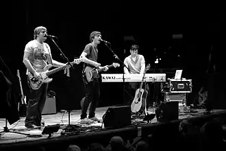 Several men performing onstage playing instruments and singing into a microphone