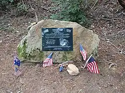 Photo of a memorial plaque fixed to a rock in El Corte de Madera preserve. Multiple small flags of the United States and Australia have been placed in front of it.