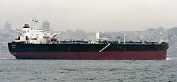 A medium size ship in front of a hazy city skyline